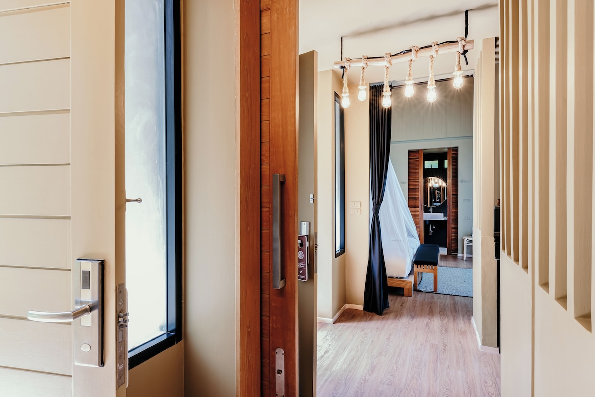 Un pasillo con una puerta de madera, un banco y una habitación con cama y cortinas.