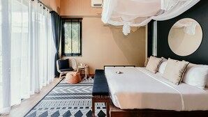Une chambre à coucher avec un grand lit, un banc, une chaise, un miroir rond et des rideaux légers.
