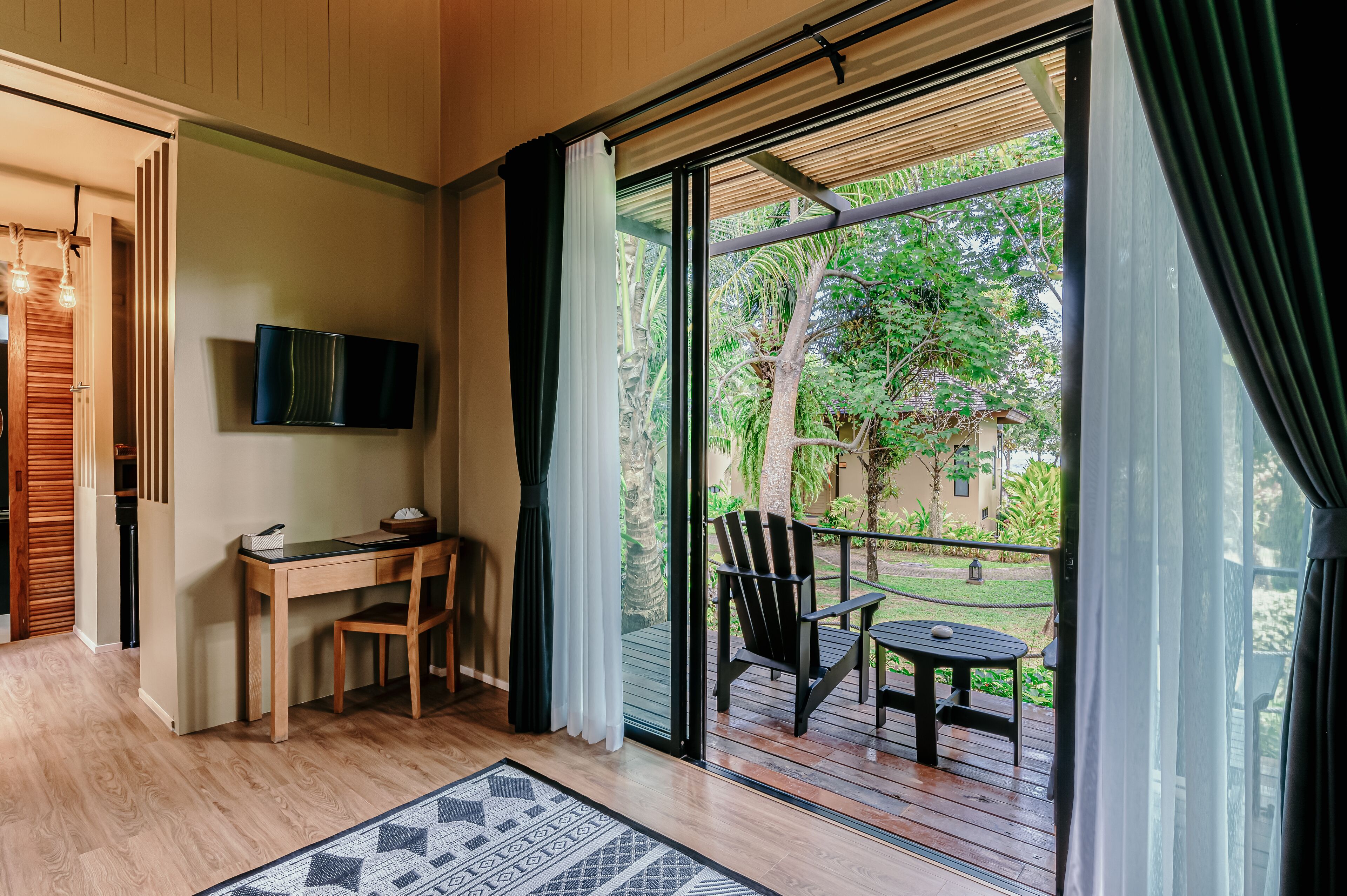 Une pièce comprenant un bureau en bois, une chaise, un téléviseur fixé au mur et un balcon avec une table et des chaises.