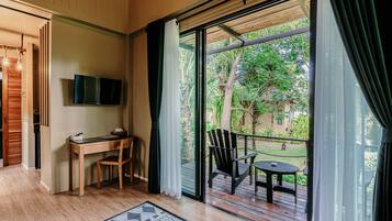 Une pièce comprenant un bureau en bois, une chaise, un téléviseur fixé au mur et un balcon avec une table et des chaises.
