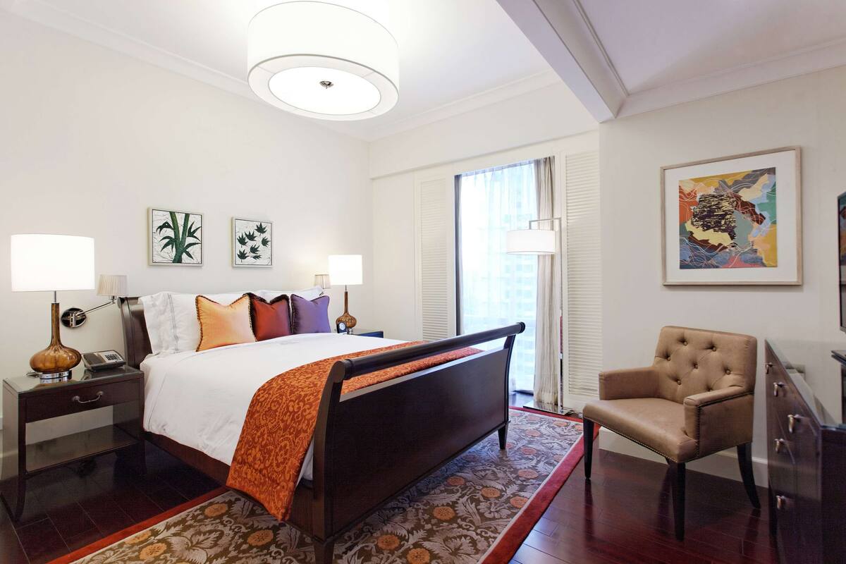 Une chambre d’hôtel avec un grand lit, une chaise, une table de chevet et une fenêtre avec des stores.