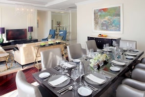 A dining area with a long table set for a meal, surrounded by modern chairs, a television, and a decorative chandelier.