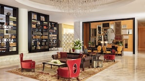 A spacious lobby with a leather sofa, red chairs, and a large chandelier. - Raffles Makati (Makati)