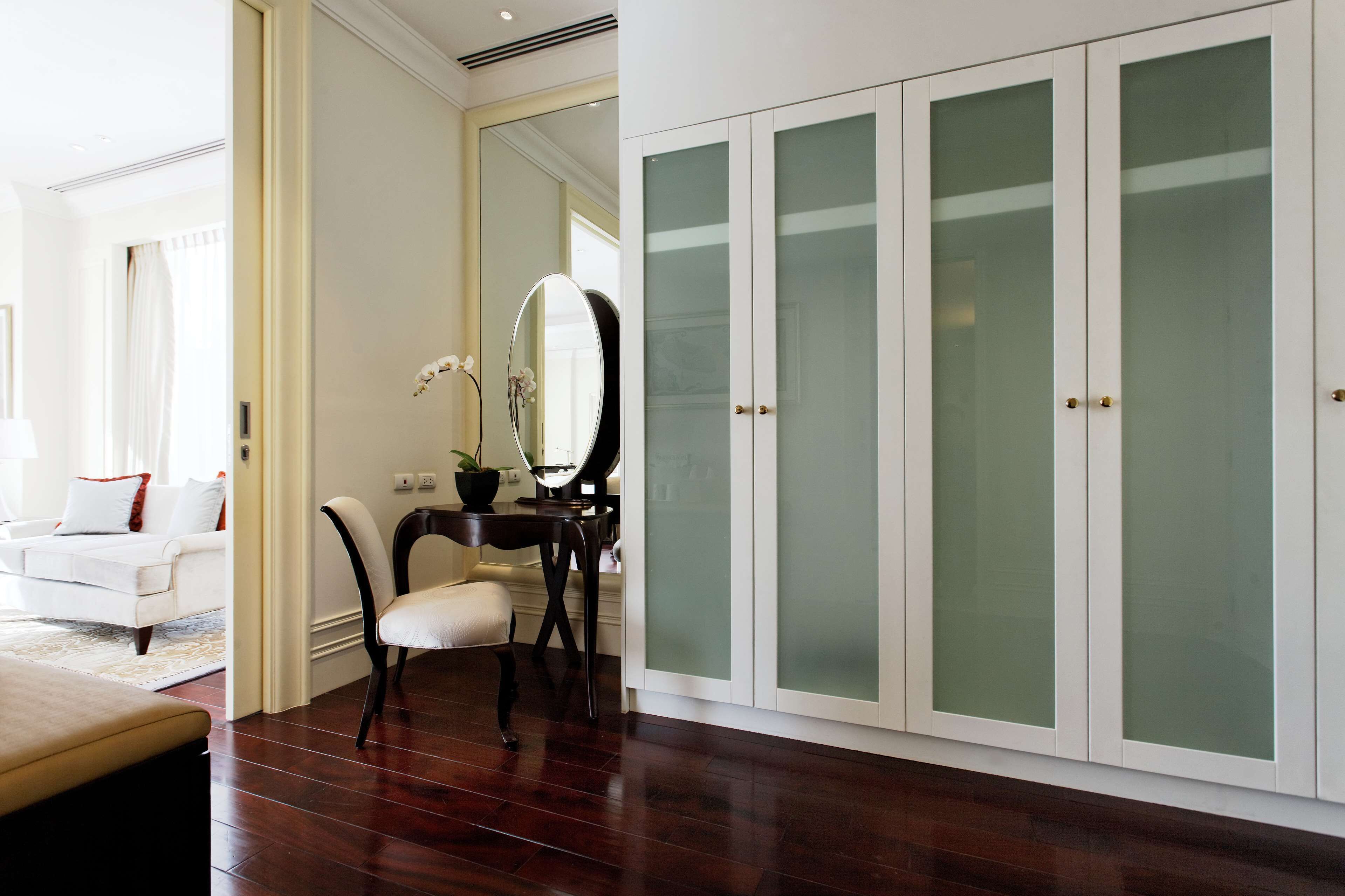A room with a white wardrobe, a mirror, a desk, and a chair.