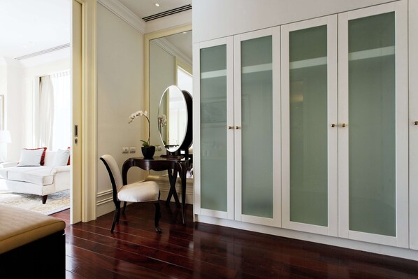 A room with a white wardrobe, a mirror, a desk, and a chair.