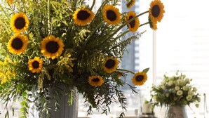 A round table with a vase of sunflowers, a blue sofa with yellow cushions, and a view of a building through a window. - Raffles Makati (Makati)