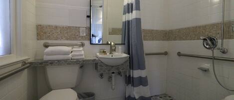 A bathroom with a toilet, sink, mirror, shower, and grab bars.