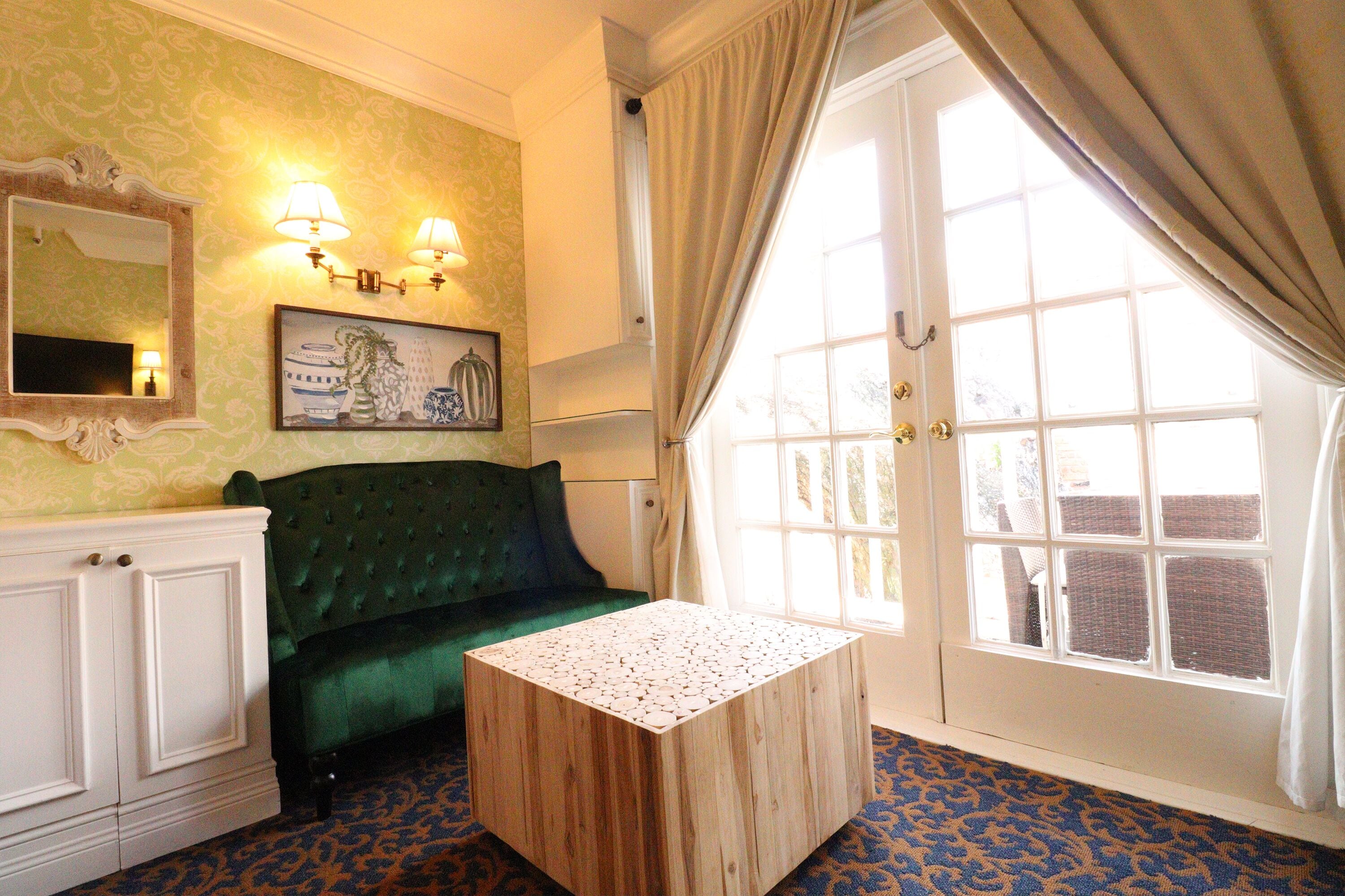 A room with a green sofa, a wooden coffee table, a mirror, wall sconces, and a window with curtains.
