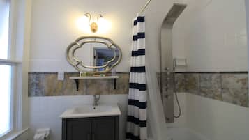 A bathroom with a shower, a sink, a mirror, and a window.