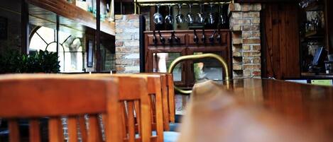 Une table à manger en bois avec des chaises, un mur en briques et des verres à vin suspendus.