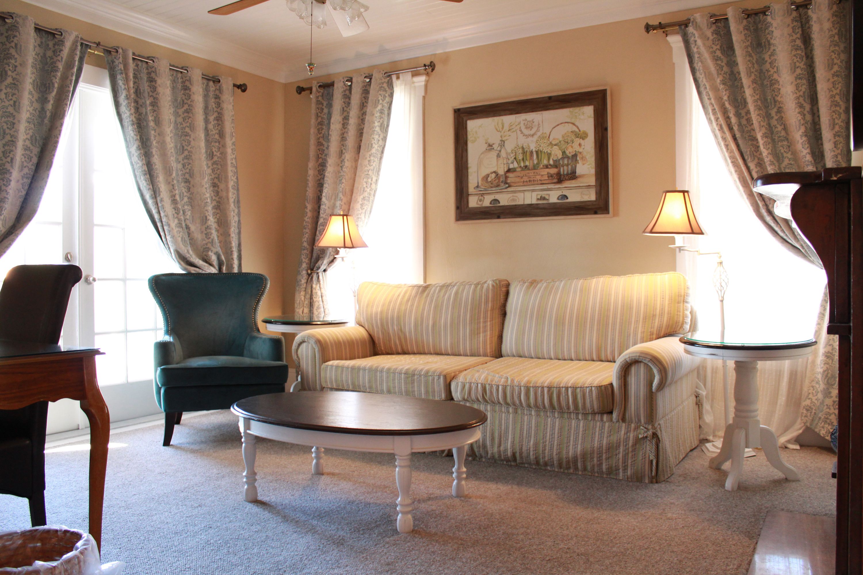 A living room with a green armchair, striped sofa, and a round coffee table. There are two lamps on side tables and a painting on the wall.