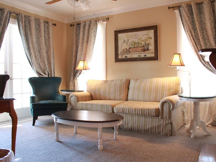 A living room with a green armchair, striped sofa, and a round coffee table. There are two lamps on side tables and a painting on the wall.