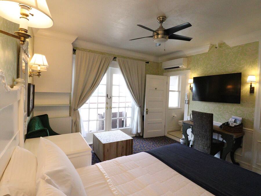 A hotel room with a bed, a desk, a chair, a television, and a ceiling fan.