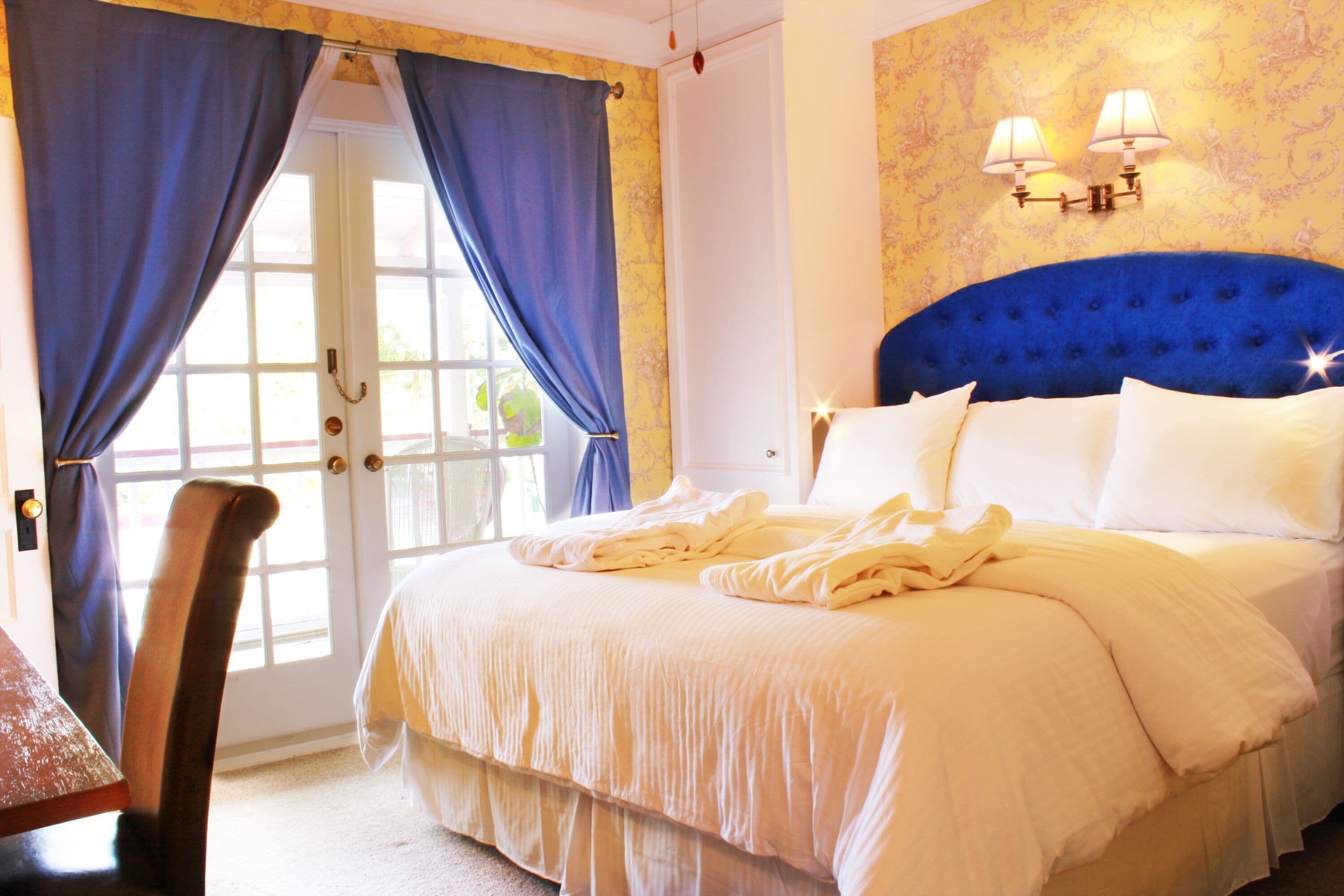 A bedroom with a large bed, a chair, a door with curtains, and wall sconces.