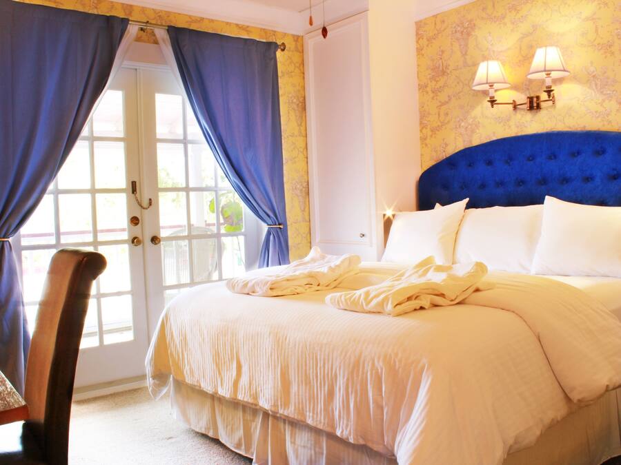 A bedroom with a large bed, a chair, a door with curtains, and wall sconces.