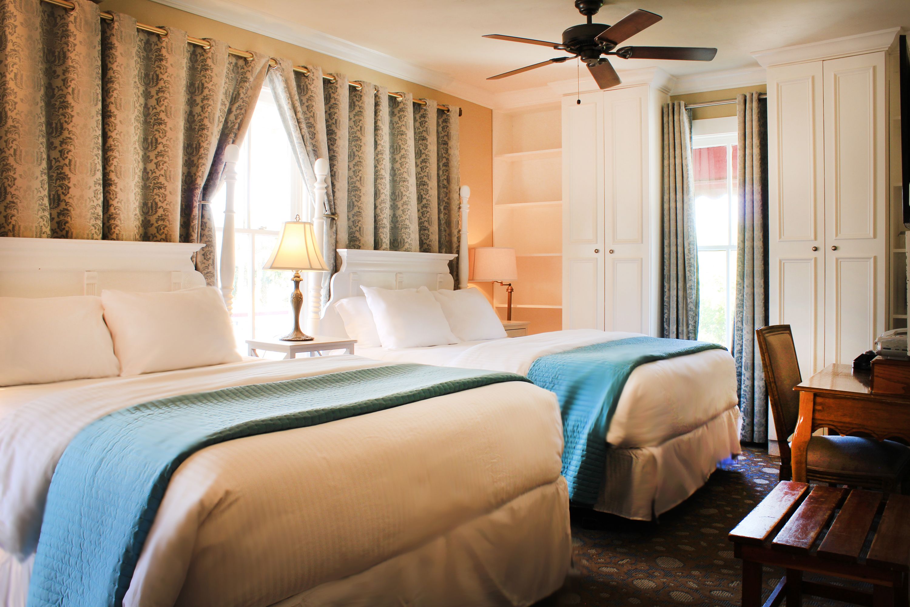 A hotel room with two beds, a desk, and a ceiling fan.