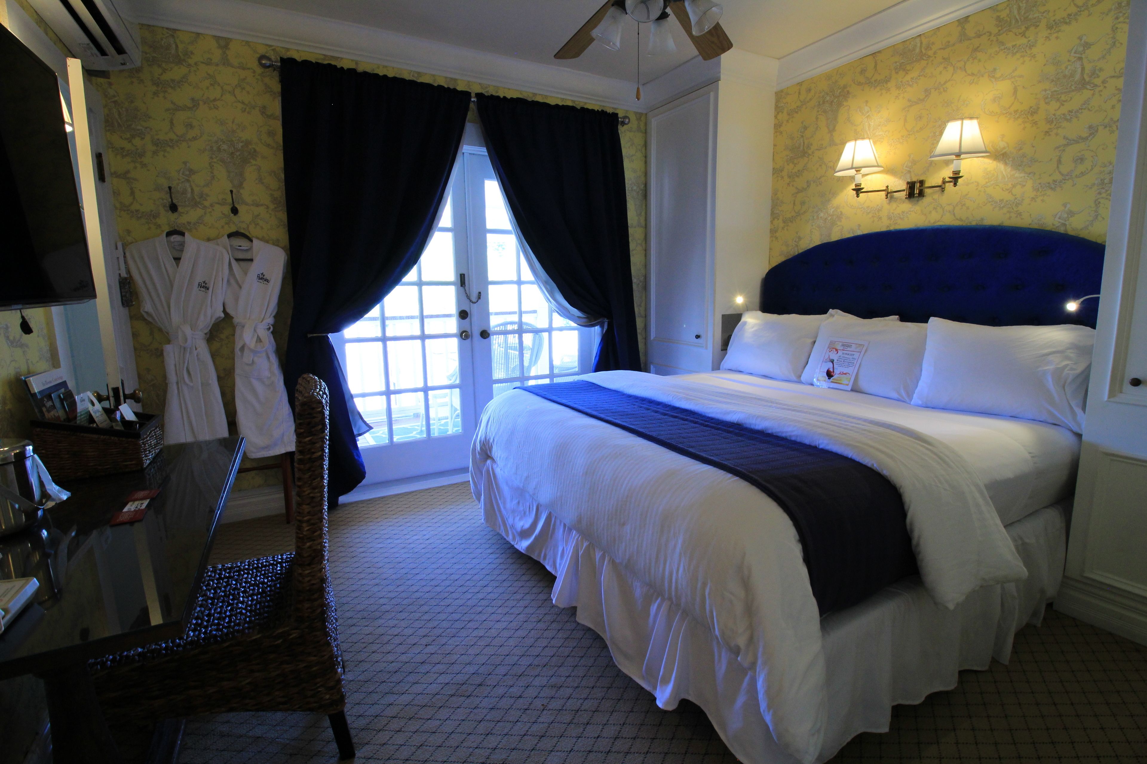 A hotel room with a large bed, a desk with a chair, and a window with curtains.