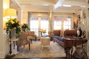 Uma sala de estar ampla, com um sofá grande, várias poltronas, uma mesa de centro e um abajur decorativo.