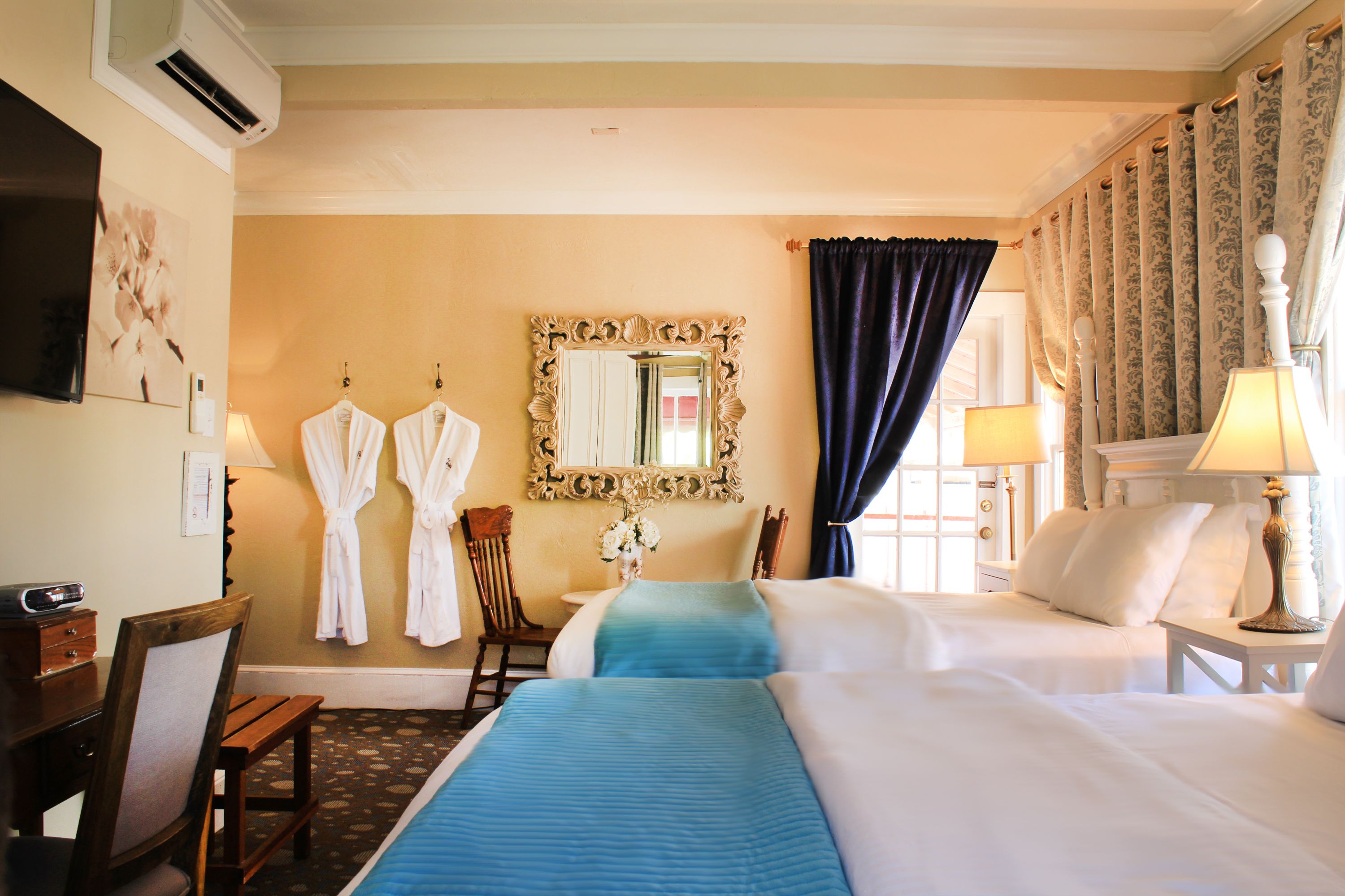 A hotel room with a large bed, a desk with a chair, a vanity with a mirror, and a TV on the wall.