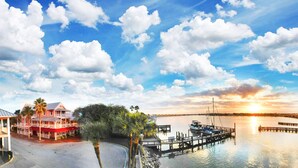 A waterfront property with a dock, a building with a red roof, and a sunset over the water. - The Riverview Hotel (New Smyrna Beach)
