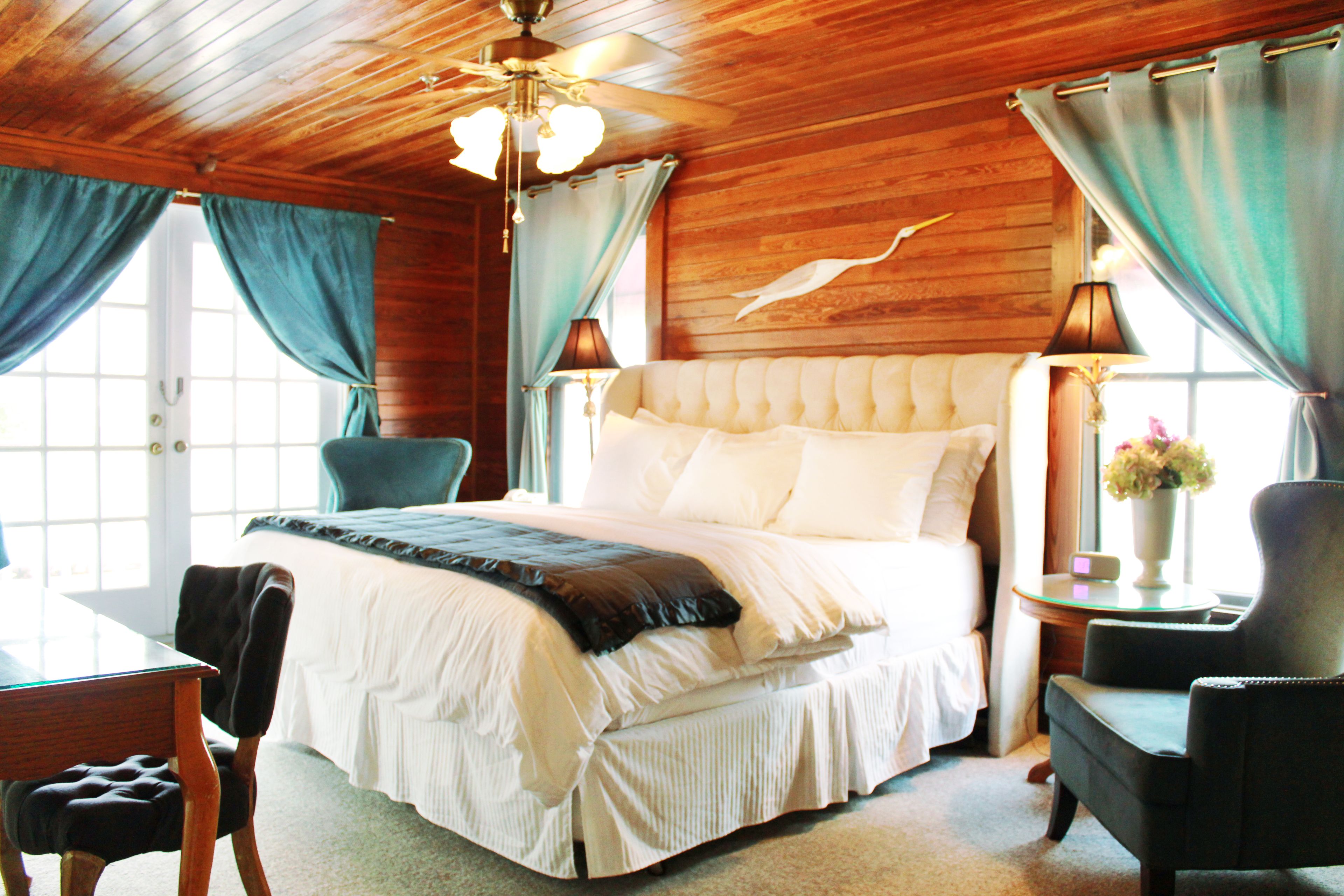Quarto com uma cama grande, teto de madeira e janela com cortinas.