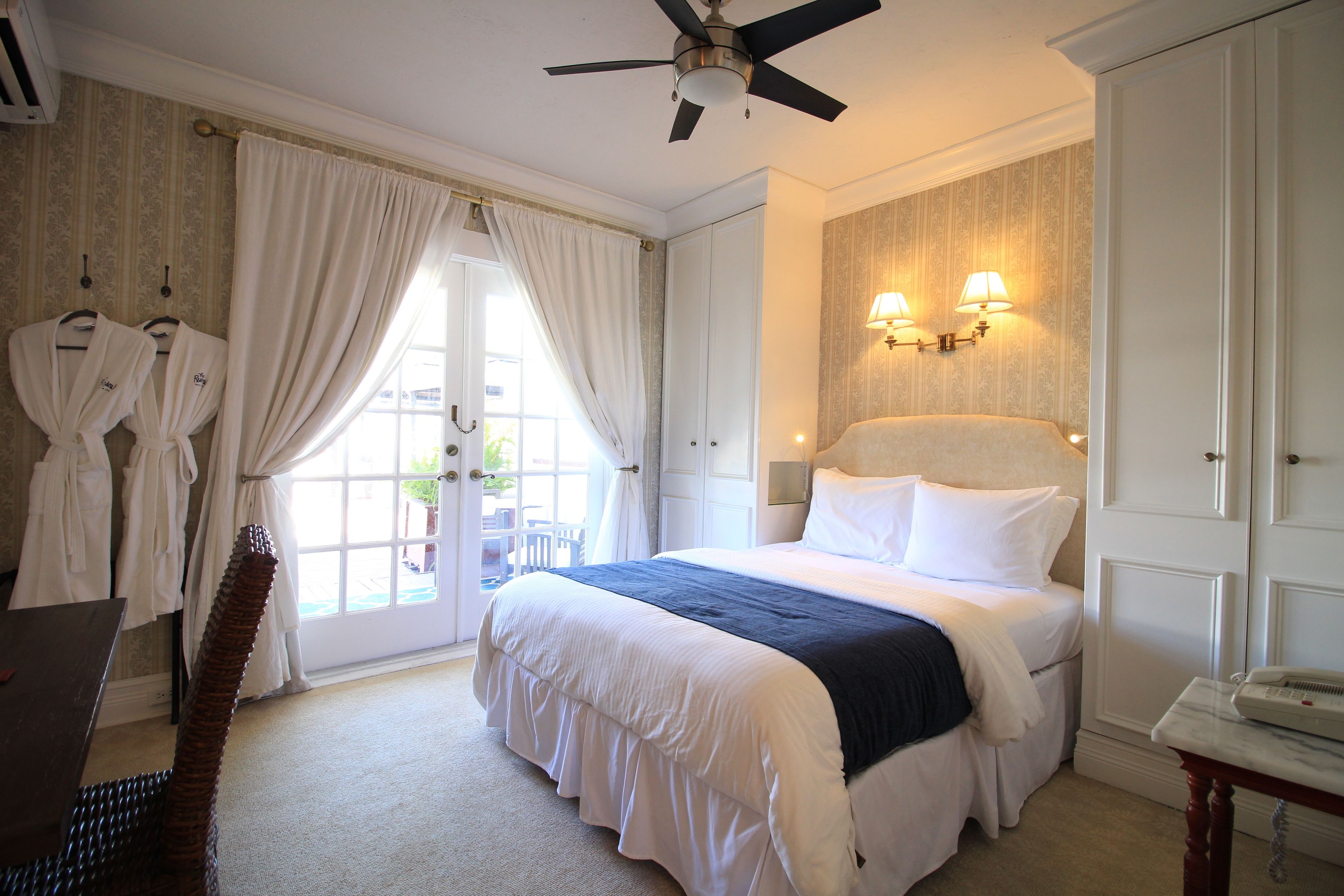 A hotel room with a bed, a desk, a chair, and a ceiling fan.