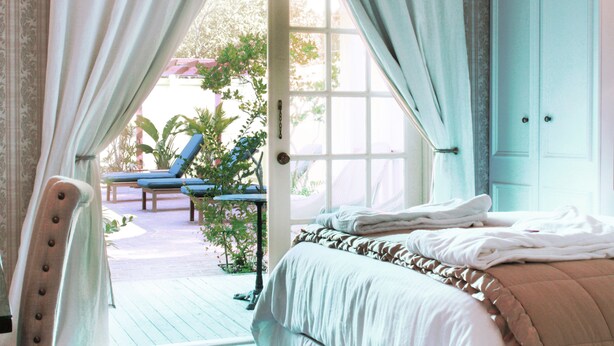 A bedroom with a bed, a chair, and a view of an outdoor area with a table and chairs. - The Riverview Hotel (New Smyrna Beach)