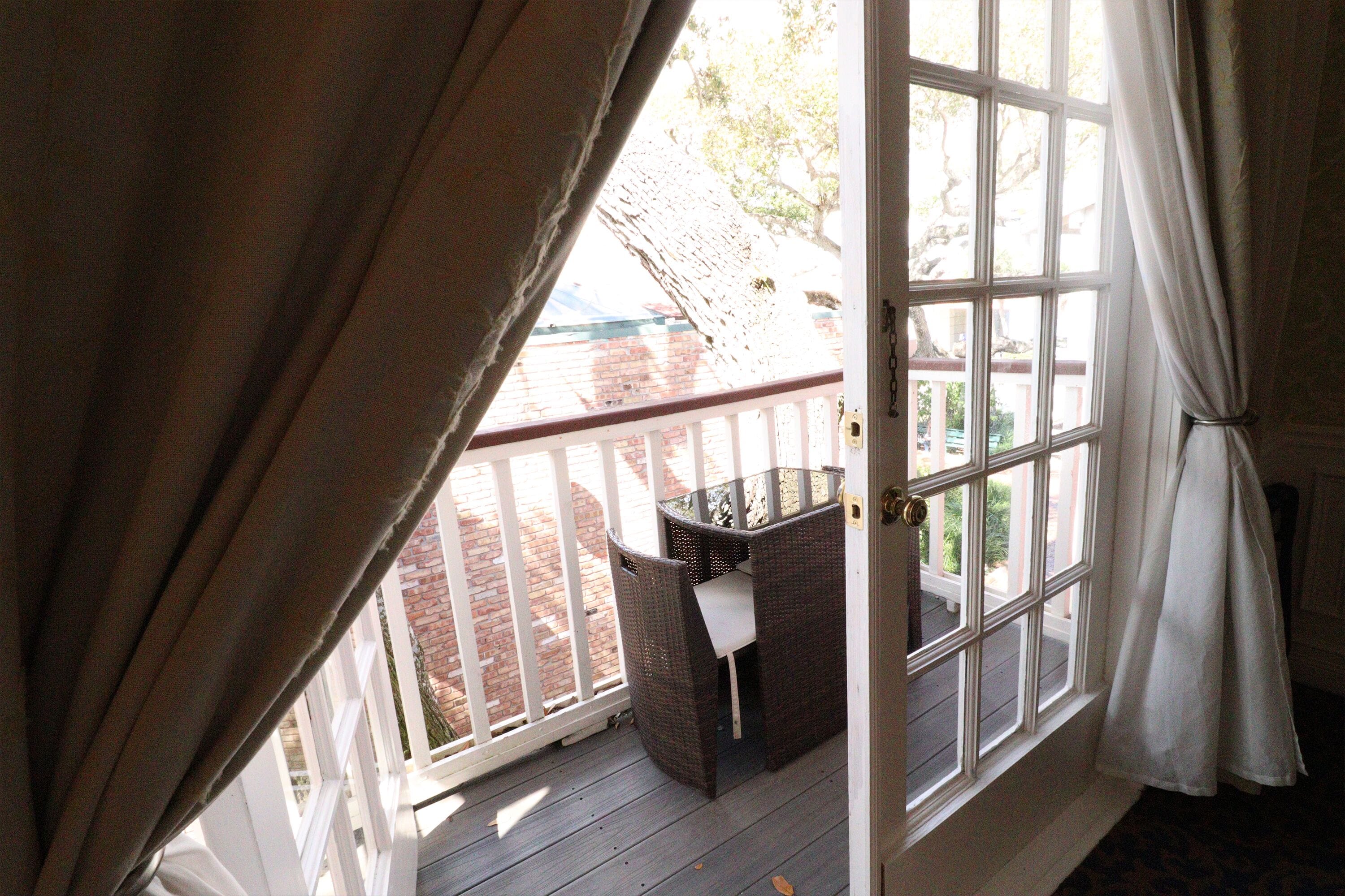 Una habitación con un ventanal grande, una silla de mimbre y una mesita.