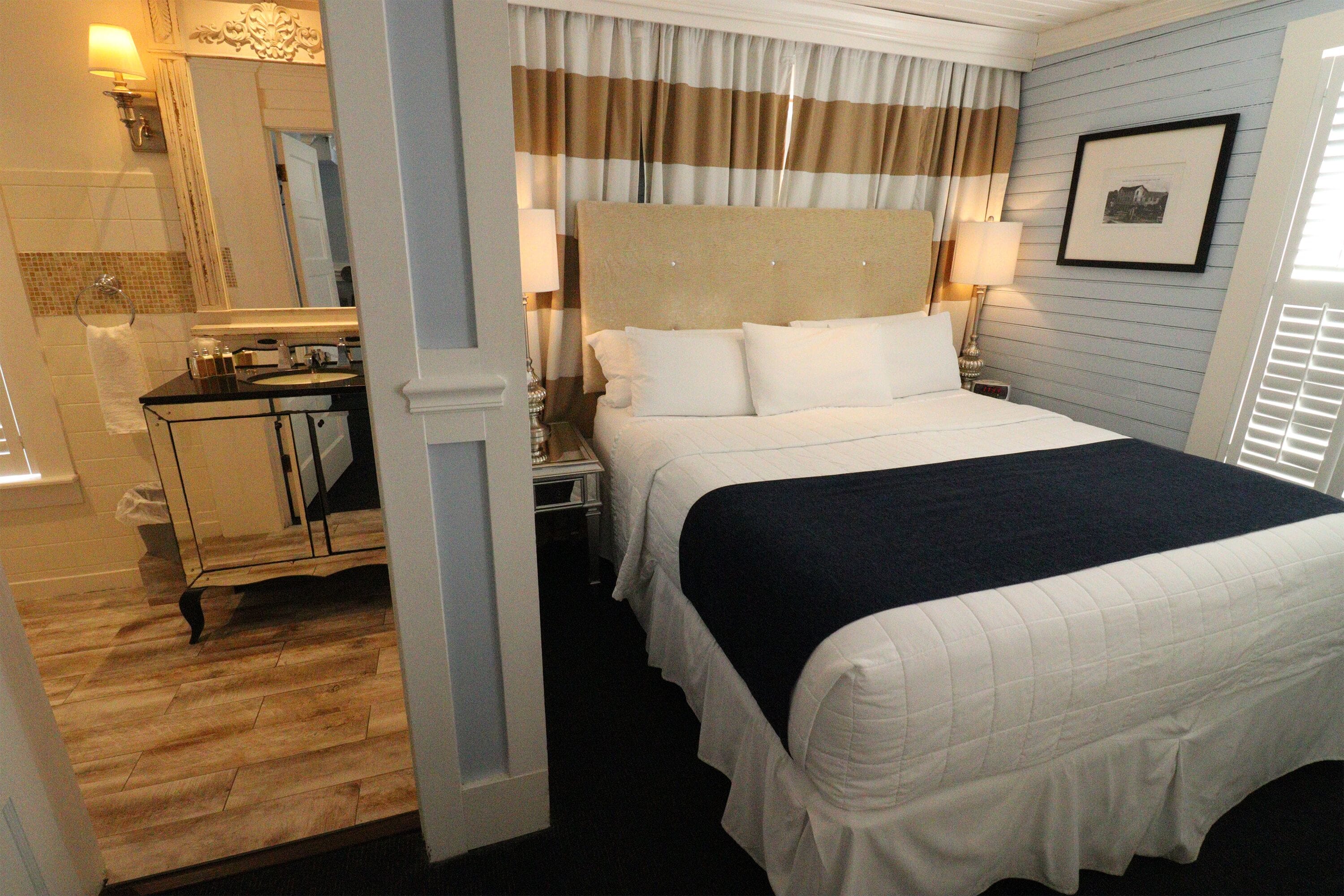Une chambre d’hôtel avec un grand lit, une coiffeuse avec un miroir et une fenêtre avec des rideaux.