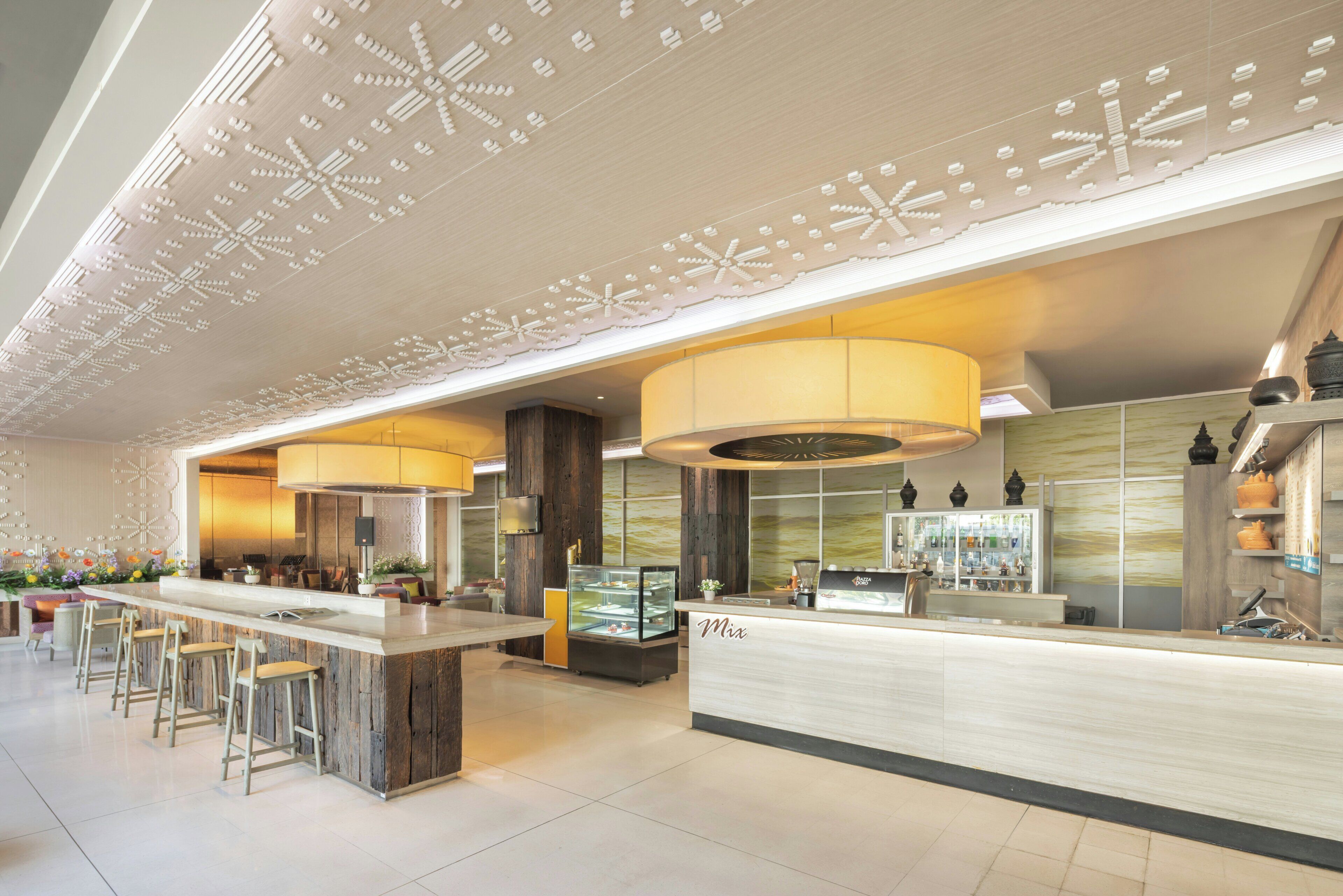 A modern hotel lobby with a reception desk, bar stools, and a large decorative ceiling.