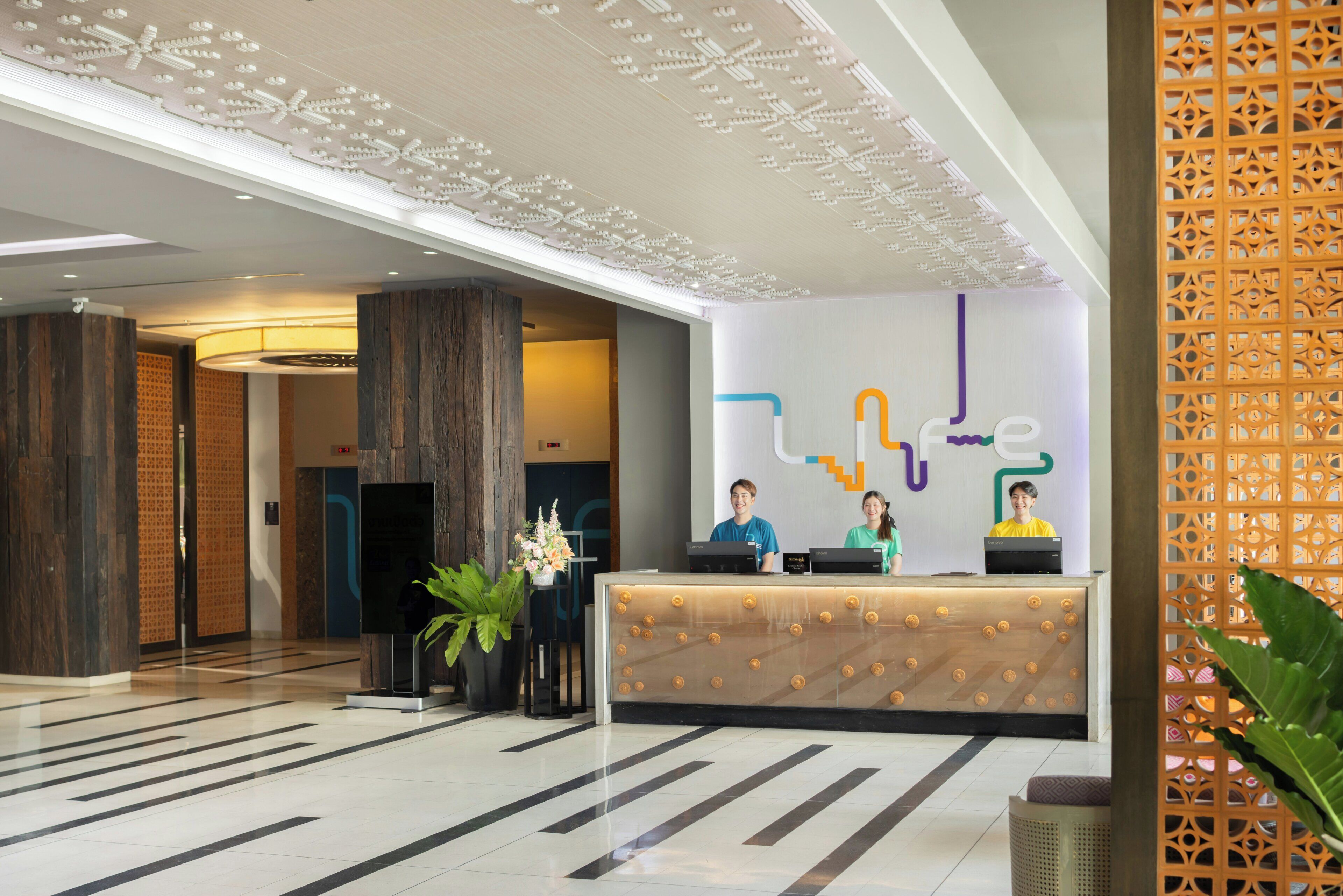 Um lobby de hotel moderno, com balcão de recepção, teto decorativo e piso estampado.