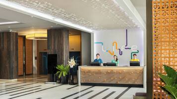 Um lobby de hotel moderno, com balcão de recepção, teto decorativo e piso estampado.