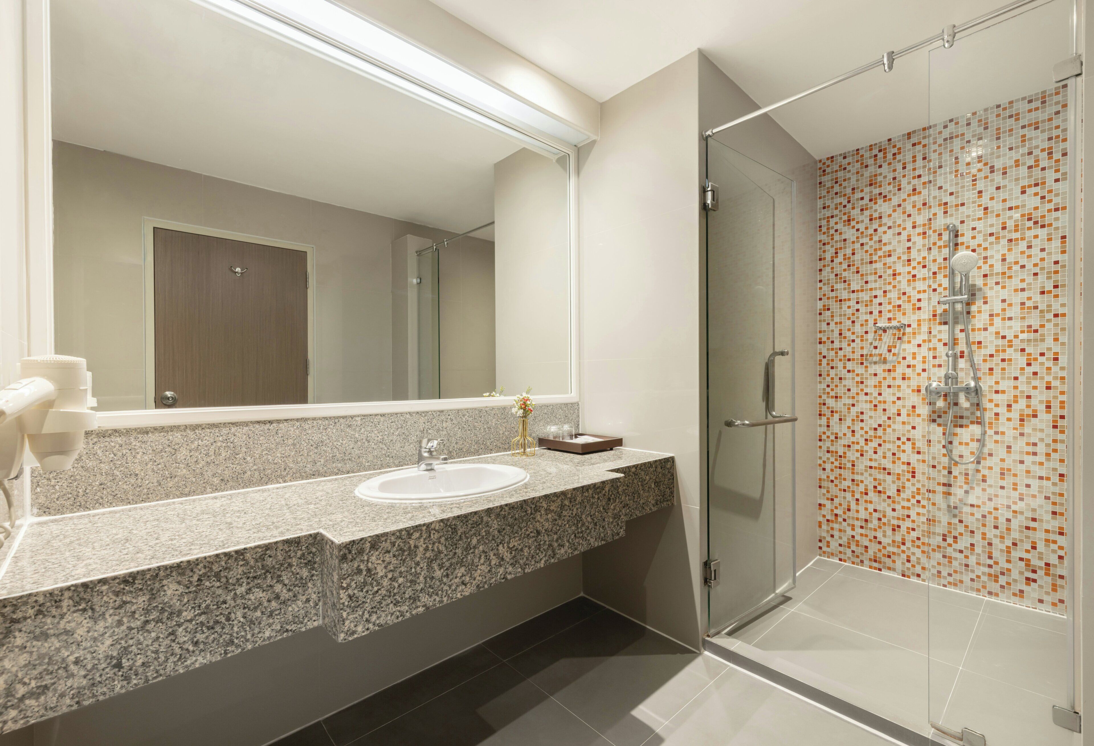 A modern bathroom with a granite countertop, a sink, a glass shower enclosure, and a tiled shower wall.