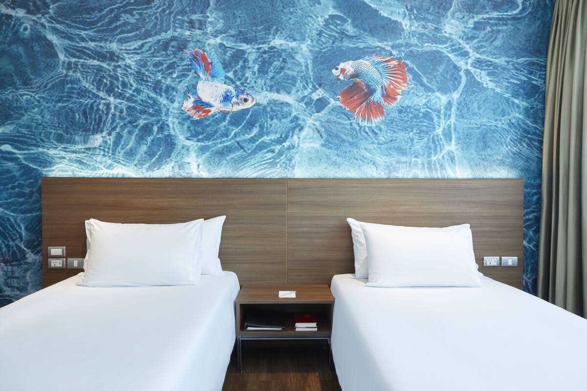 Habitación de hotel con dos camas, cabecero de madera y un mural de peces en la pared.