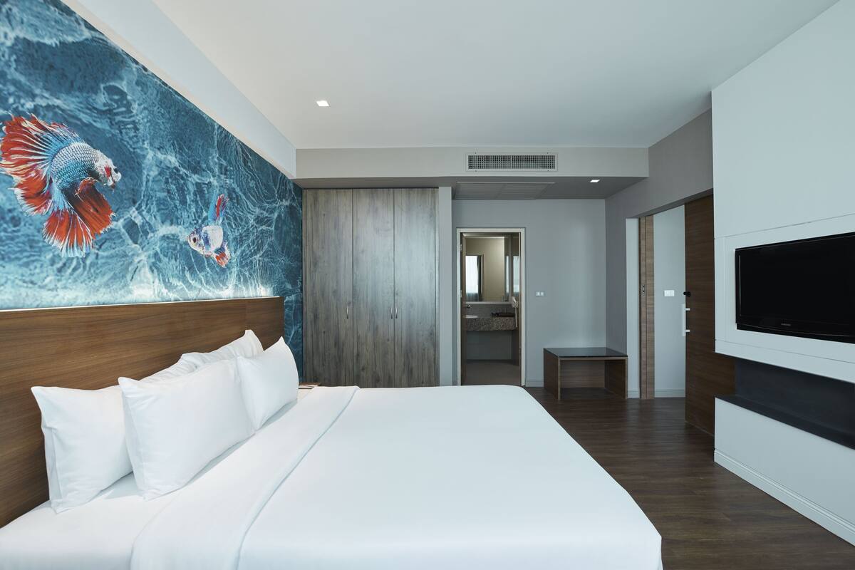 Un hotel moderno con una cama grande, un televisor montado en la pared y un mural decorativo con motivos de peces.