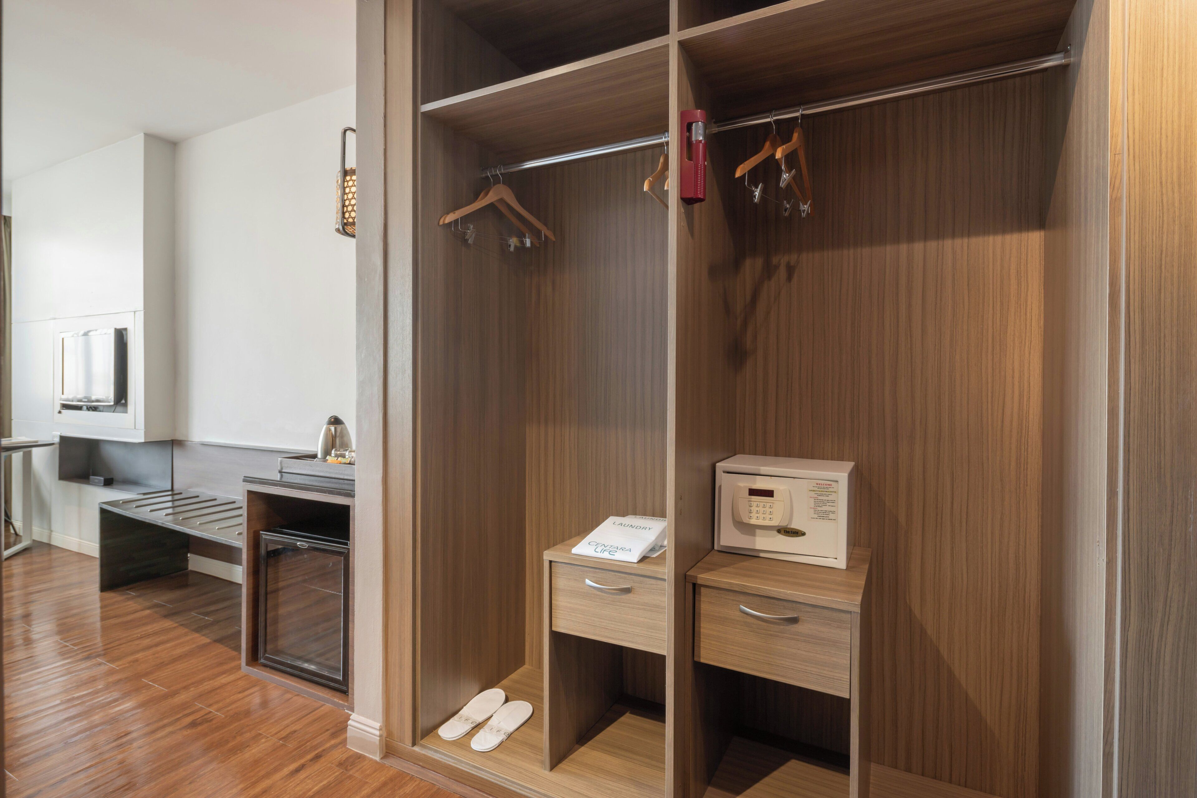 Un armario con puertas de madera, una barra para colgar ropa, un electrodoméstico blanco pequeño y un par de zapatillas en el suelo.