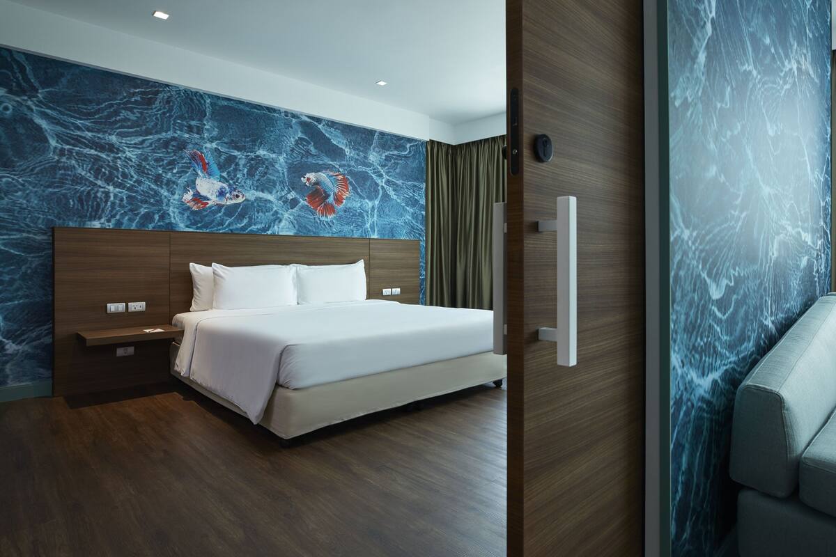 Habitación de hotel moderna con una cama grande, cabecero de madera y una pared de mármol azul con motivos de peces.
