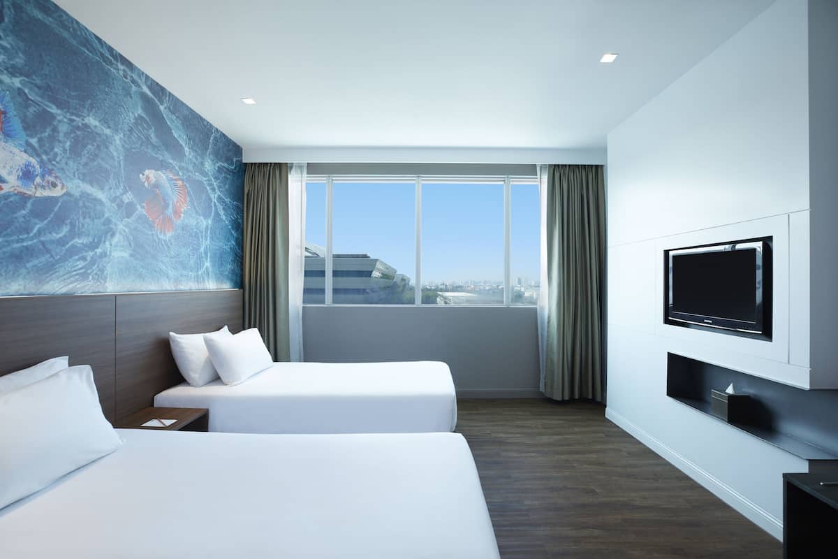 Habitación de hotel con dos camas, un ventanal con vistas a la ciudad, un televisor montado y una obra de arte de mármol en la pared.