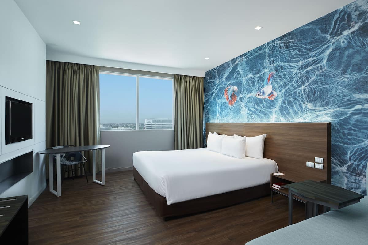 Habitación de hotel con una cama grande, televisión, escritorio y vista a la ciudad.