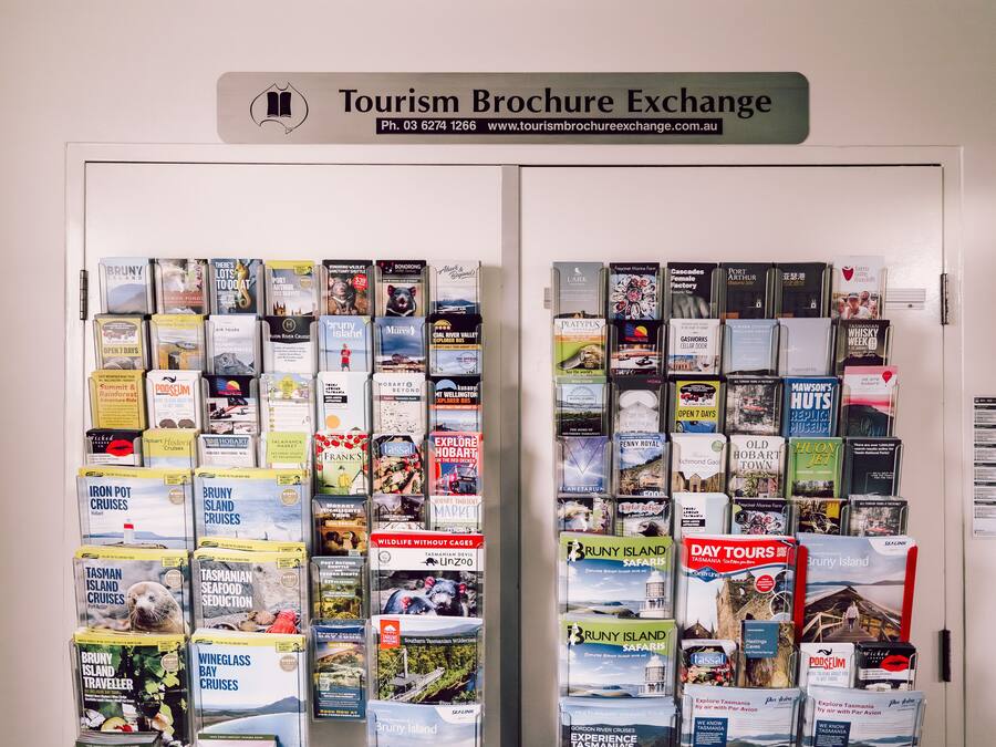 Una pared con un cartel que dice "Intercambio de Folletos Turísticos" y una colección de folletos para diversos recorridos y destinos.