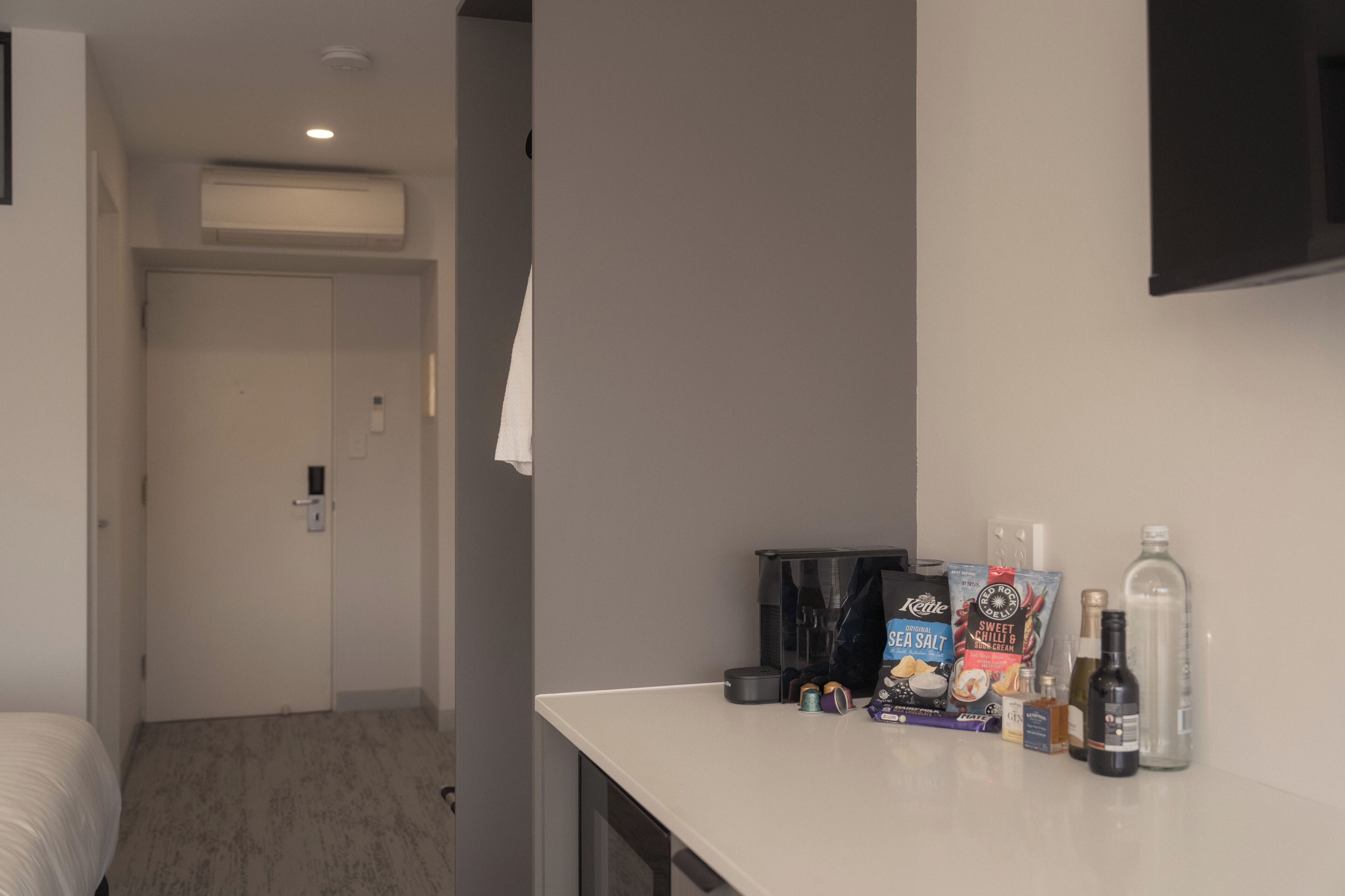 Habitación de hotel con cama, una mesita con aperitivos y bebidas, un televisor montado en la pared y una puerta que da a otra habitación.