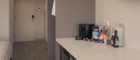 Habitación de hotel con cama, una mesita con aperitivos y bebidas, un televisor montado en la pared y una puerta que da a otra habitación.
