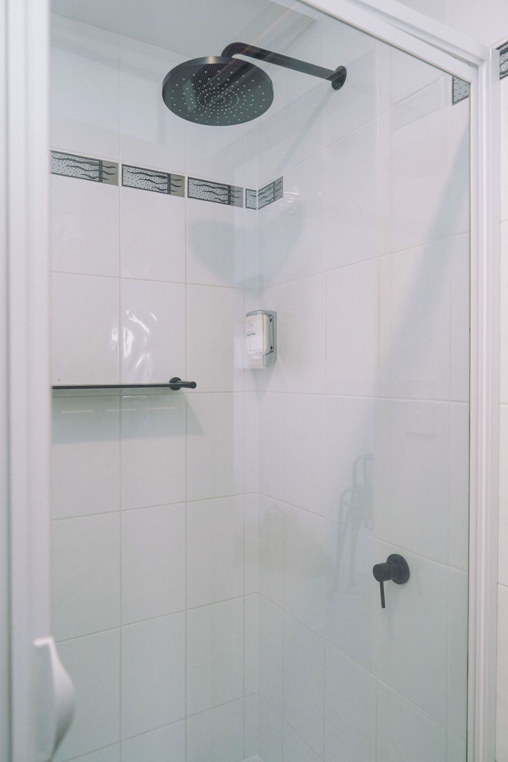 A shower with a rain showerhead, a towel rack, and a soap dispenser.