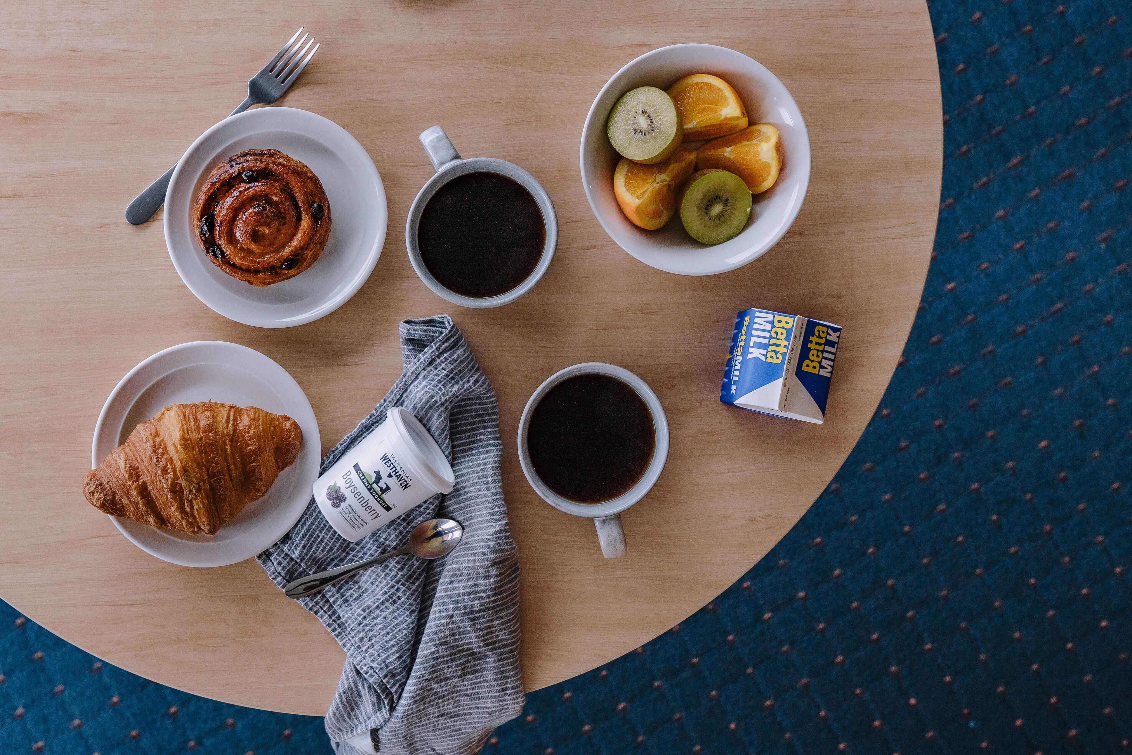 A breakfast setting with croissants, coffee, and fruit on a wooden table.