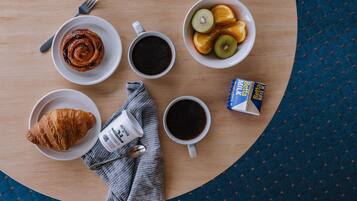 A breakfast setting with croissants, coffee, and fruit on a wooden table.