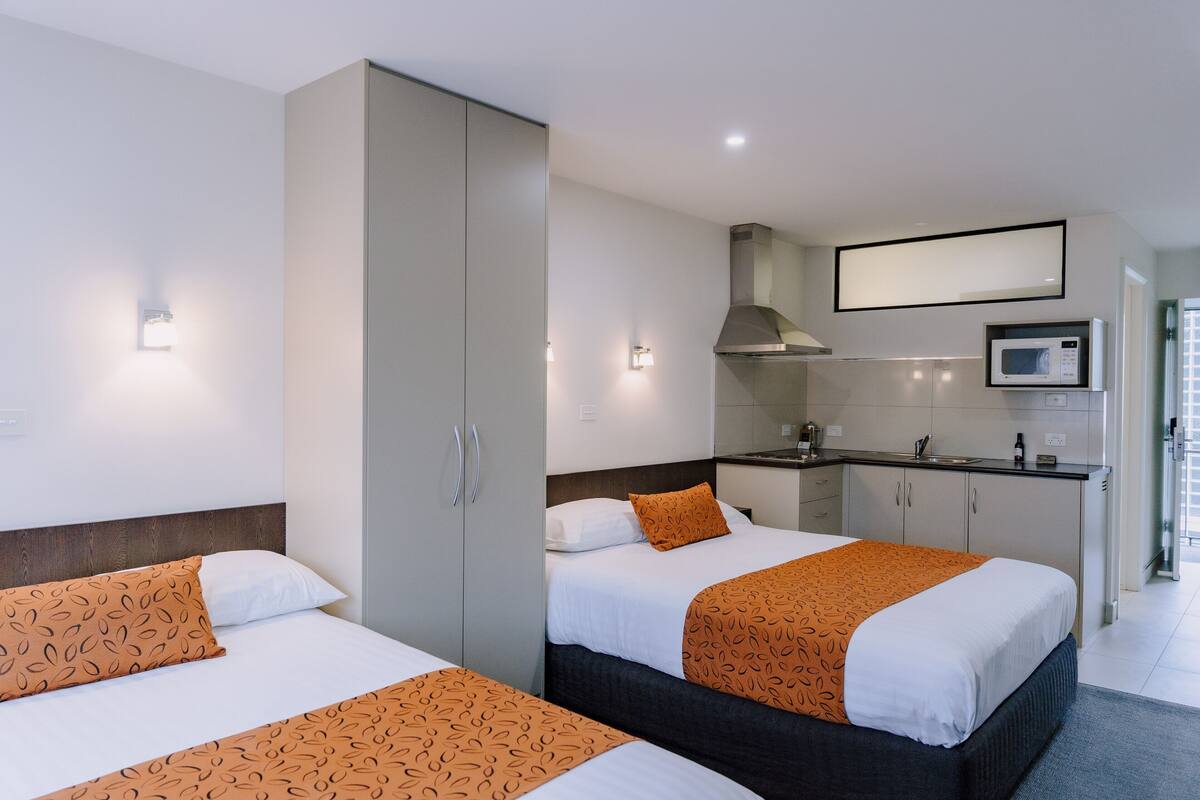 Quarto de hotel com duas camas, cozinha compacta e banheiro.