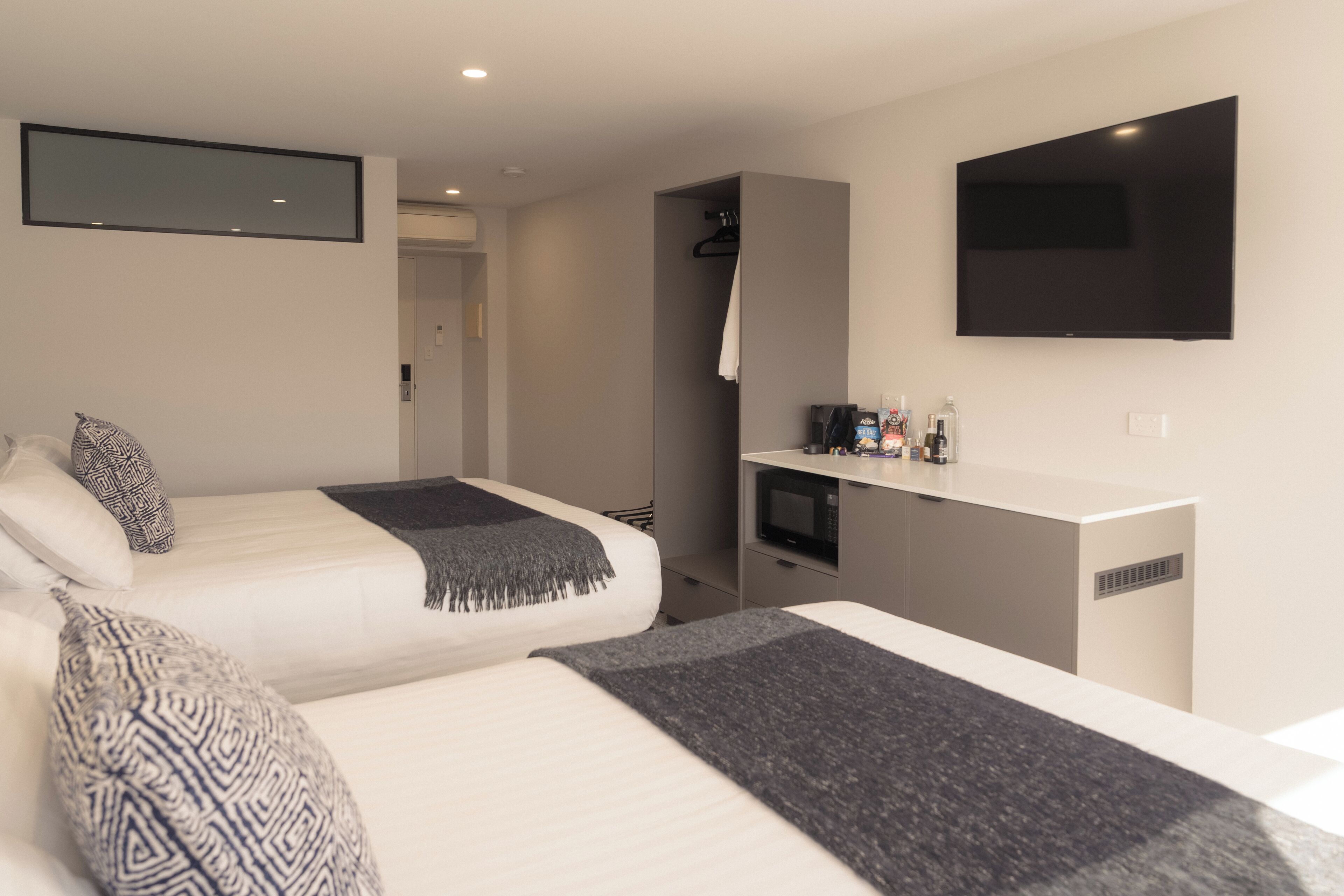 Habitació d'hotel moderna amb dos llits, televisió de pantalla plana, microones i una cuineta petita.