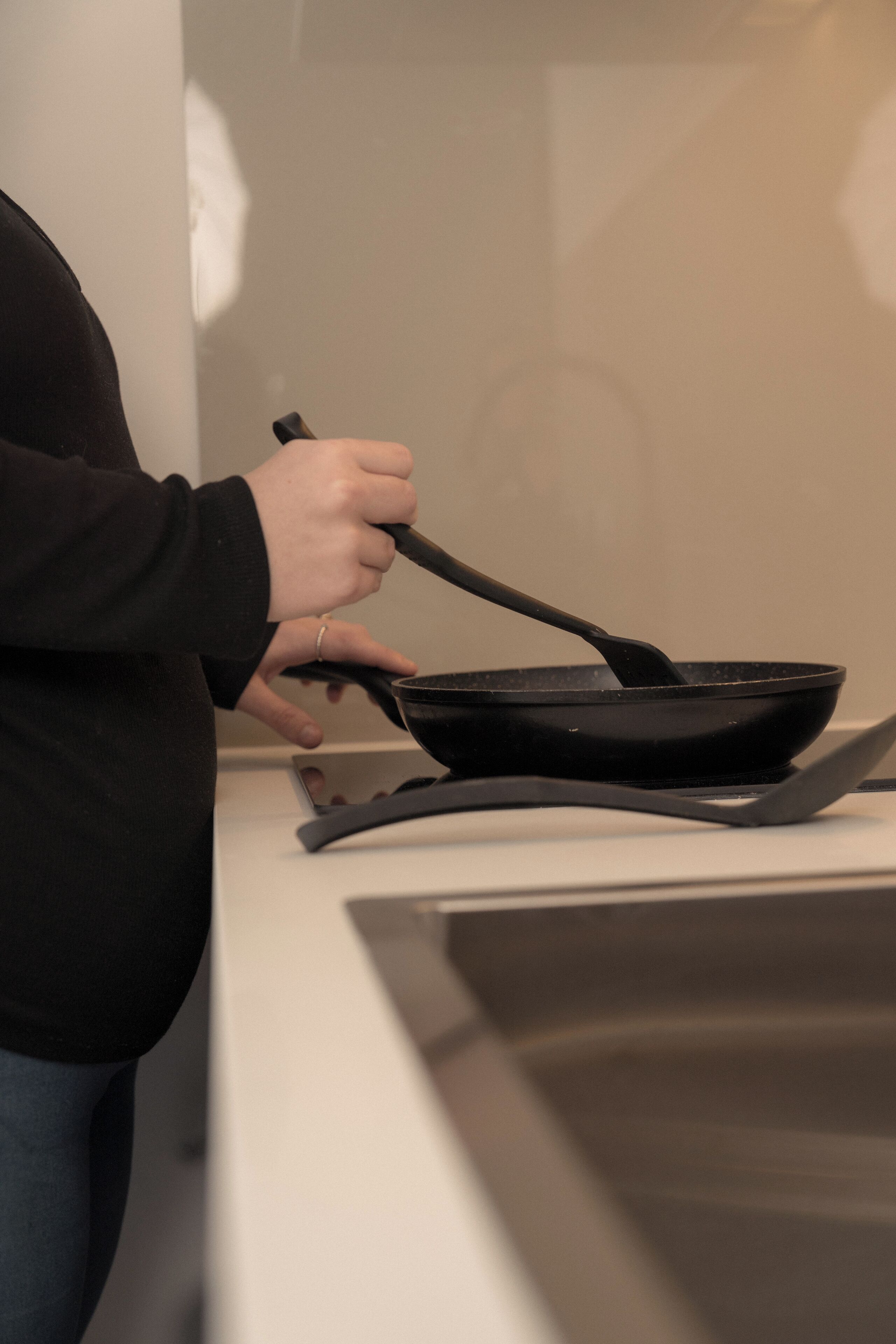 A person cooking in a kitchen with a stove and a frying pan.