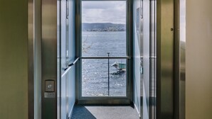 Un ascensor con puerta de vidrio, barandal de metal y vista a un cuerpo de agua a través del cristal.