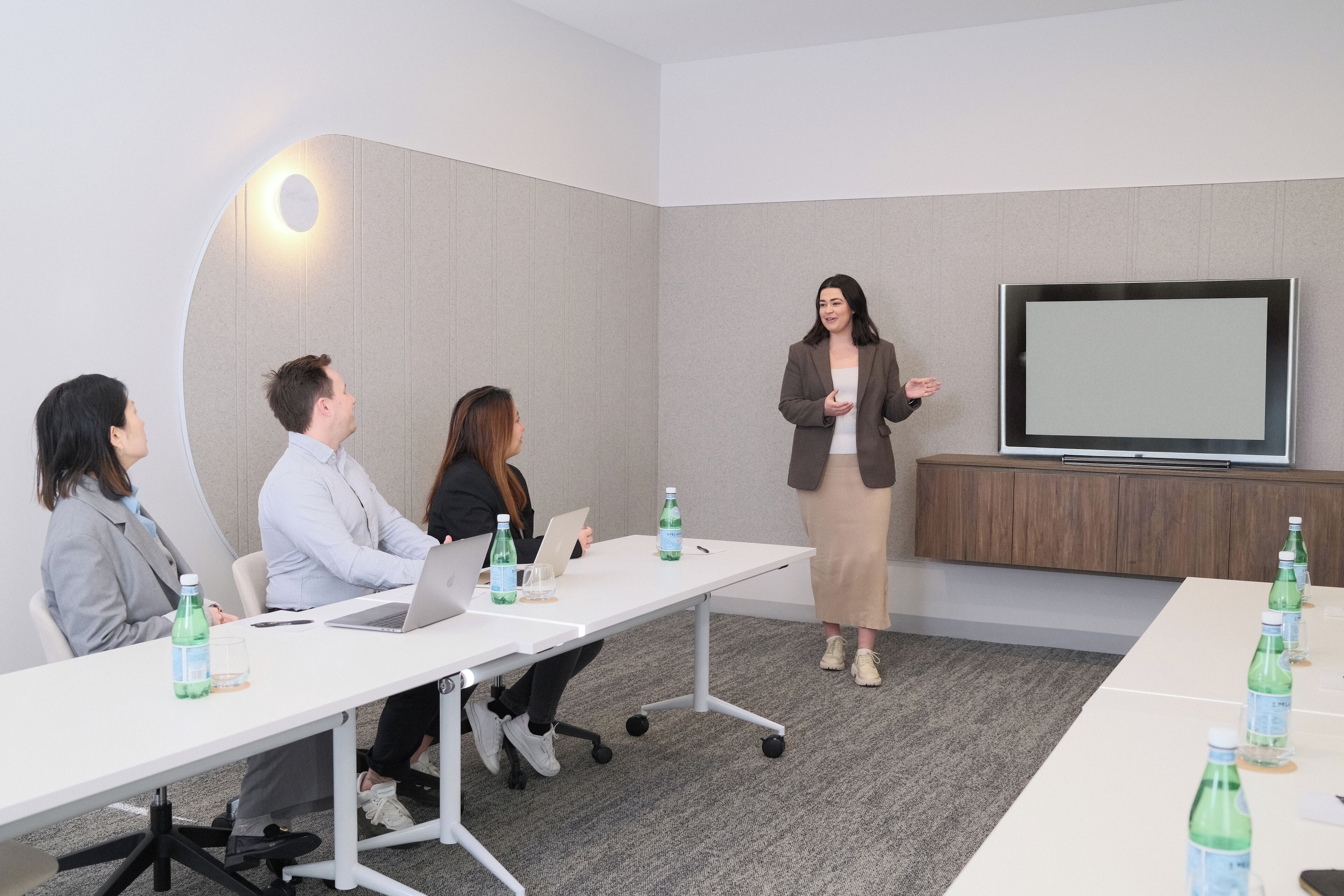 A conference room with a white table, four people seated, and one person standing presenting.